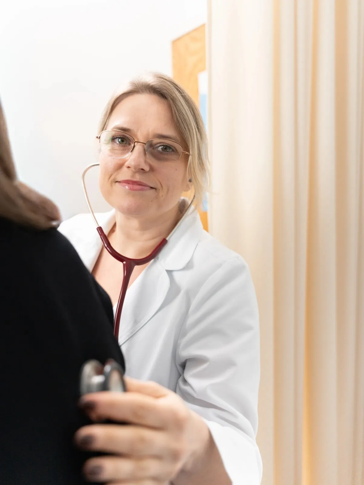 Anna Mekhed wearing a stethoscope and glasses while interacting warmly with a patient.