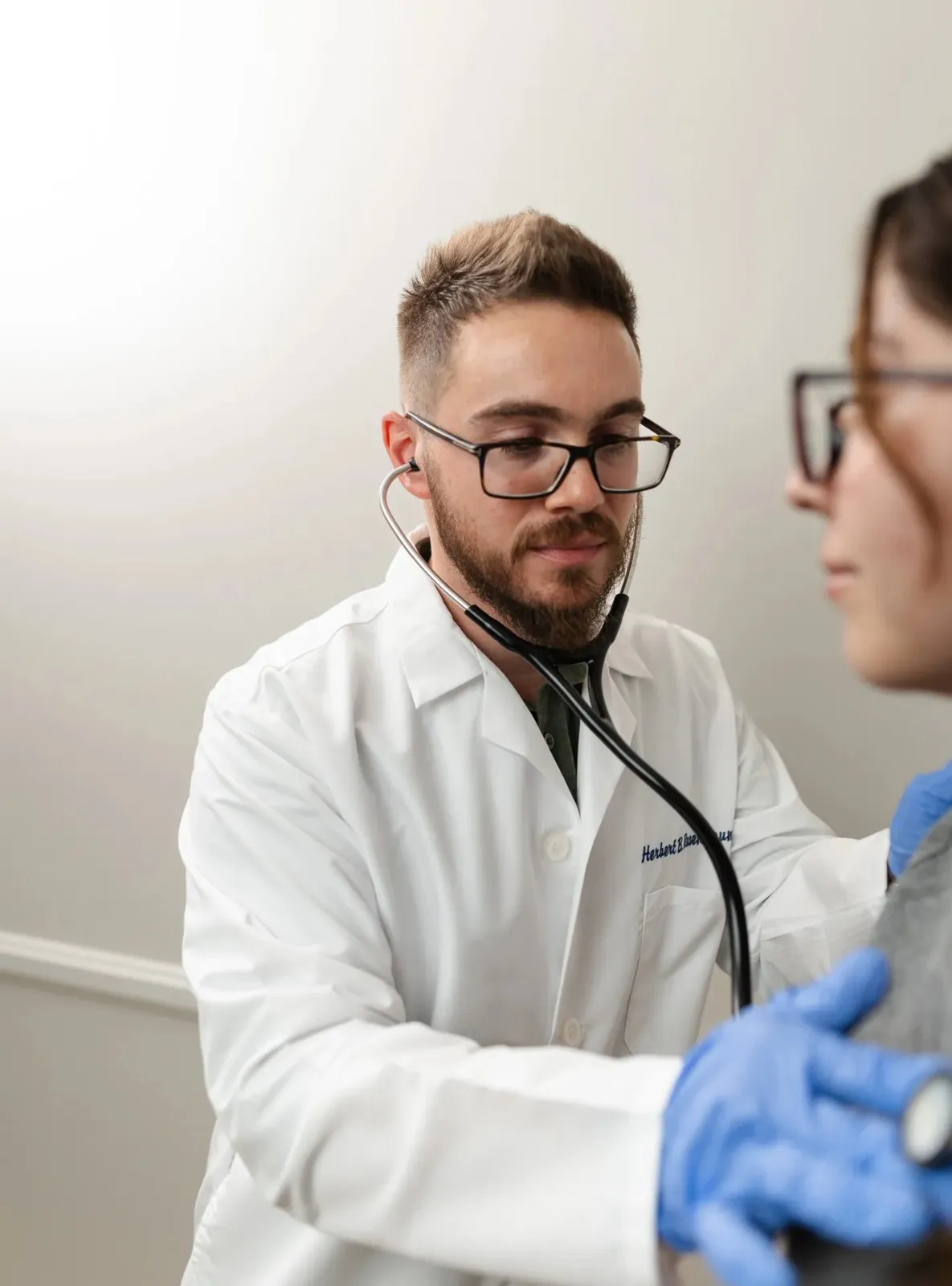 Dr. Herbert Rosenbaum wearing blue medical gloves and a lab coat while preparing for a patient examination.