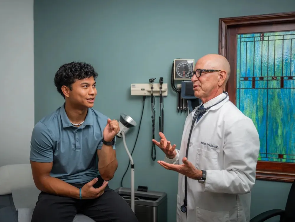A professional portrait of Dr. William Padilla in medical attire within the clinic hallway.