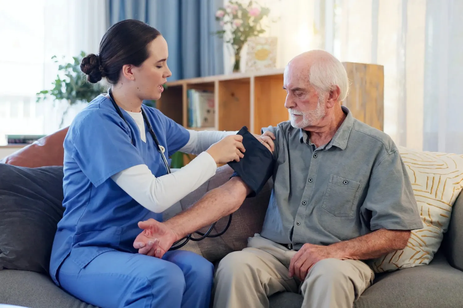 A female nurse in blue scrubs providing senior care to adult man